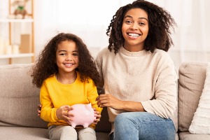 Mother and daughter smiling on couch with piggy bank in hand
